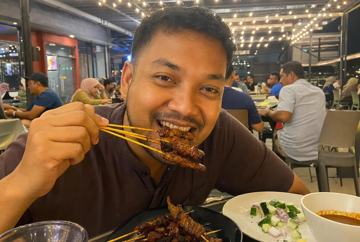 A happy diner biting satay straight off the skewer at a lively Rumah Rasa night table